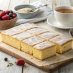 Golden kefir sheet cake sliced into squares, served with berries and tea
